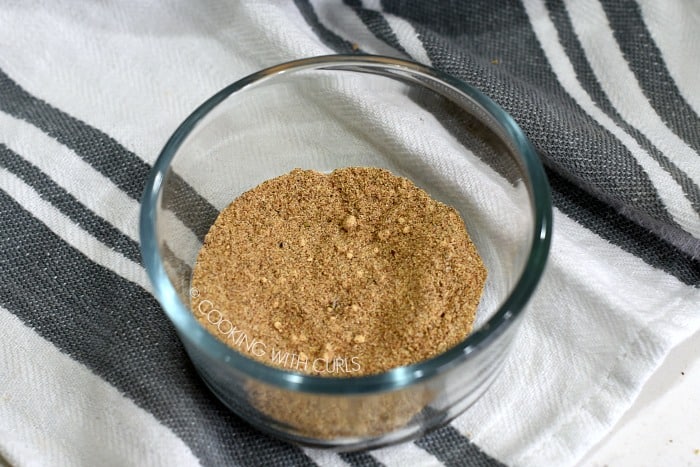 A small glass bowl with a mixture of spices sitting on a gray and white striped towel 