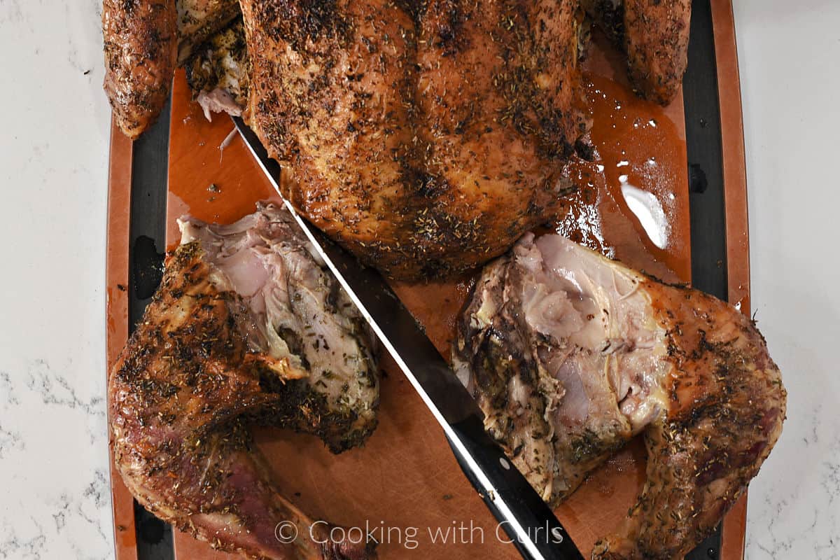 A spatchcock turkey laying on a cutting board with the legs cut off with a carving knife.