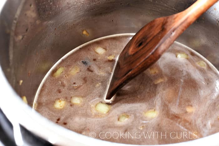 A wooden spoon scraping the bottom of the pressure cooker to remove all of the cooked on bits. 