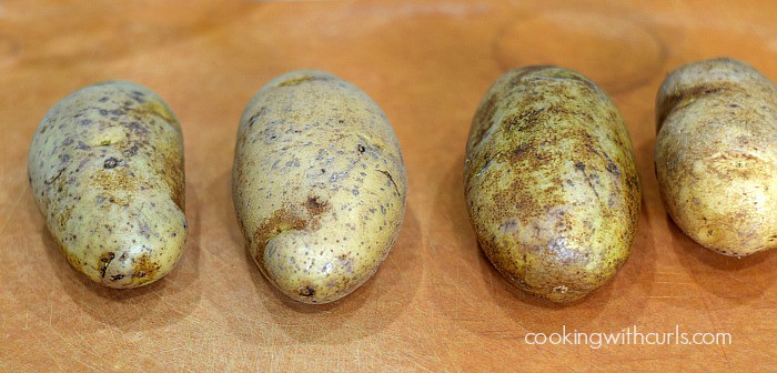 Four large russet potatoes on a cutting board.