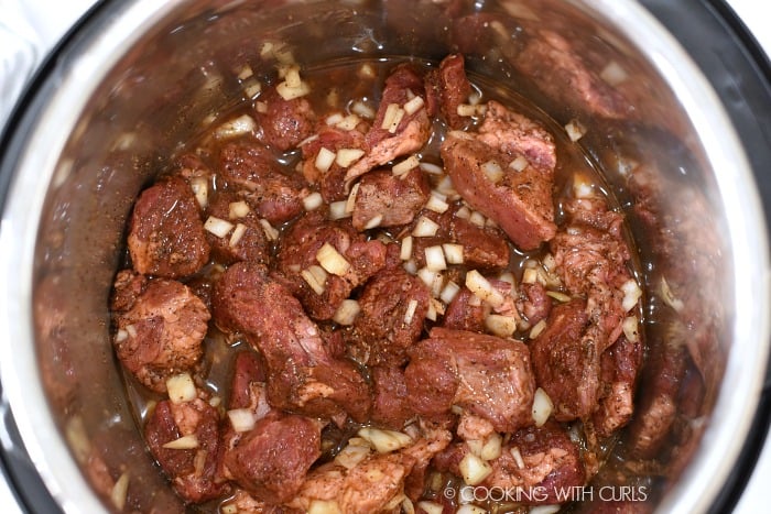 Beef chunks in a pressure cooker with beef stock, chopped onions and coffee.