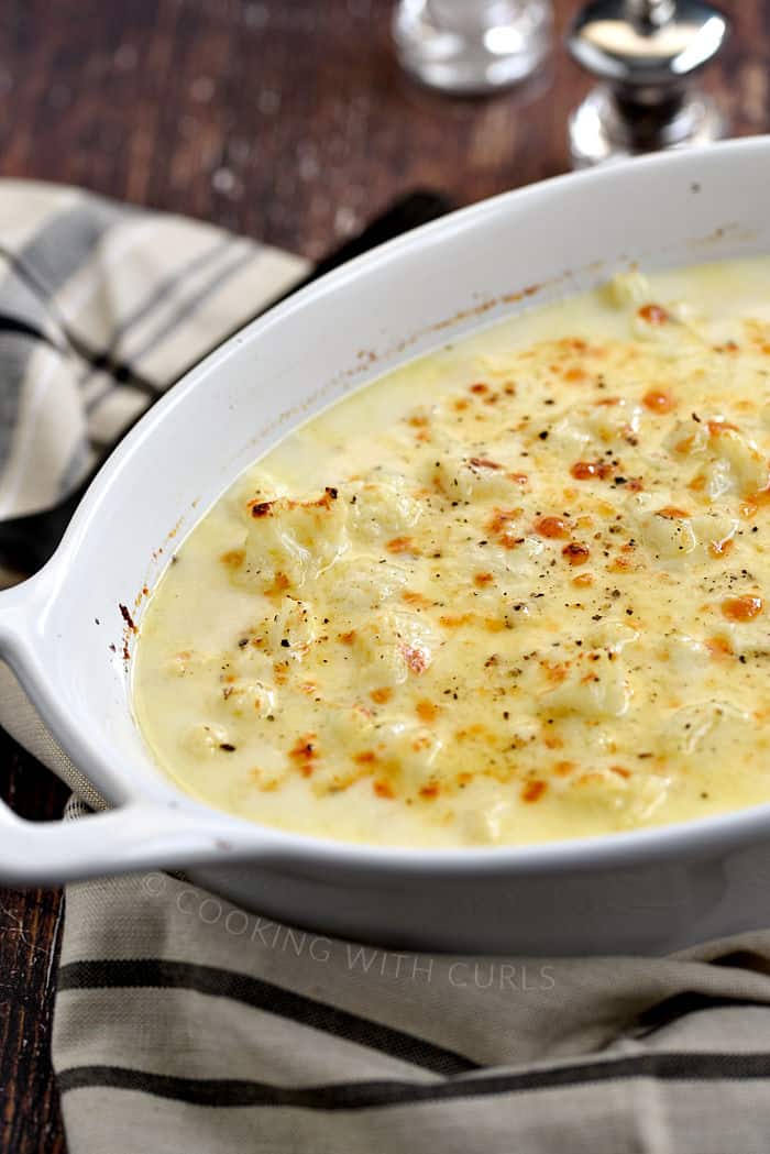 Cheese topped cauliflower in a creamy sauce in a white baking dish with salt and pepper shakers in the background.