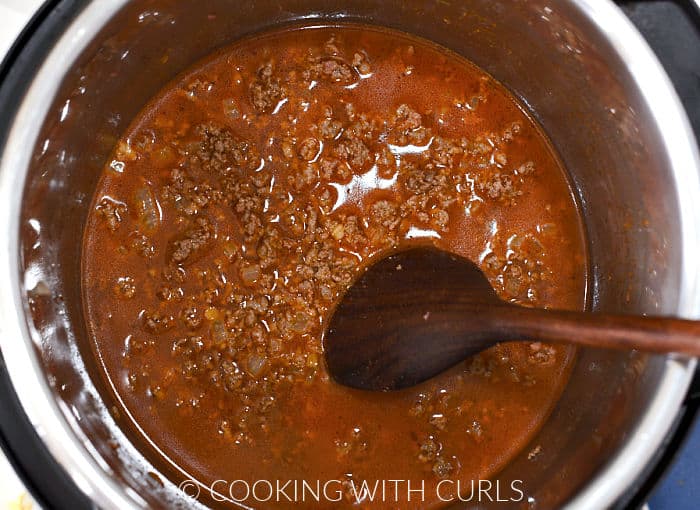 Chicken stock and ground beef in an instant pot with a wooden spoon on the right side. 