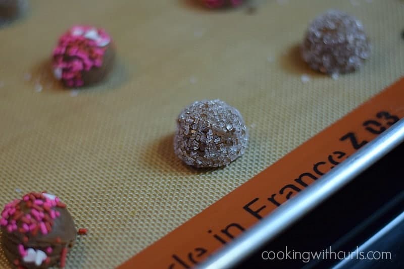 Chocolate Peanut Butter cookie dough rolled in sprinkles and placed on a silicone lined baking sheet.