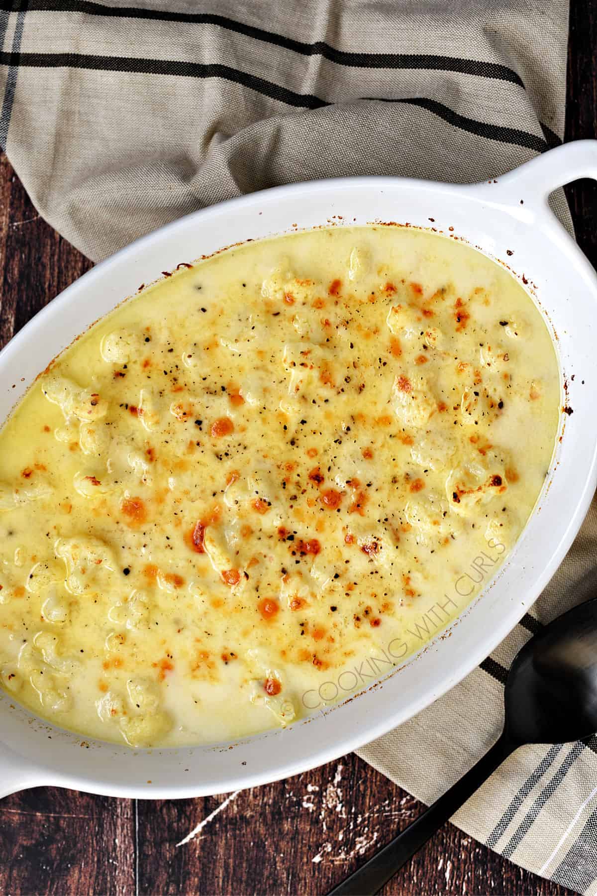 Looking down on an oval baking dish filled with baked, cheesy cauliflower.