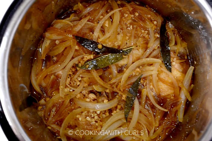 Cooked chicken thighs, adobo sauce, sliced onions, and split bay leaves in a pressure cooker.