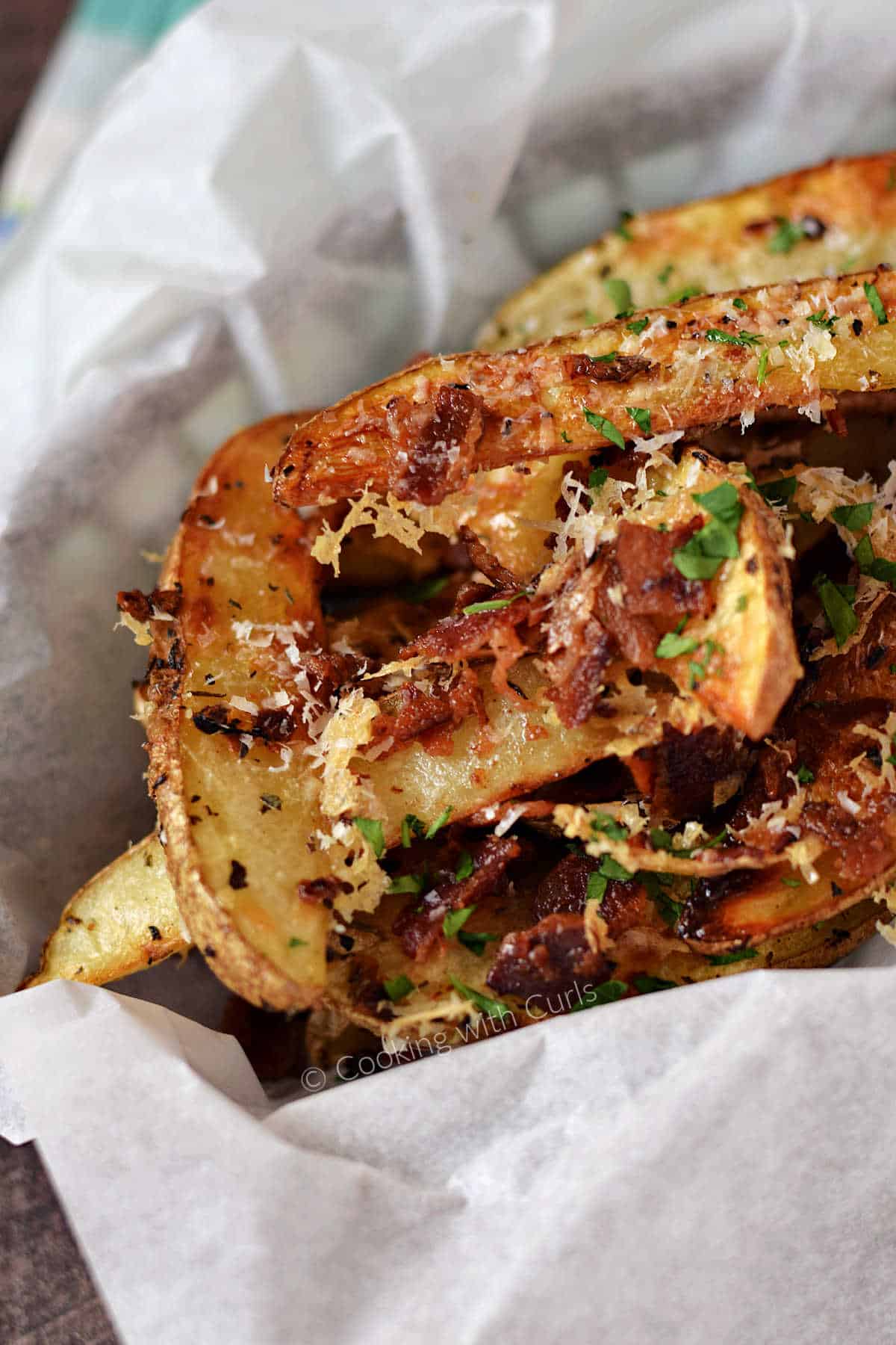 Baked potato wedges topped with Parmesan cheese, bacon, and herbs in a parchment lined basket.