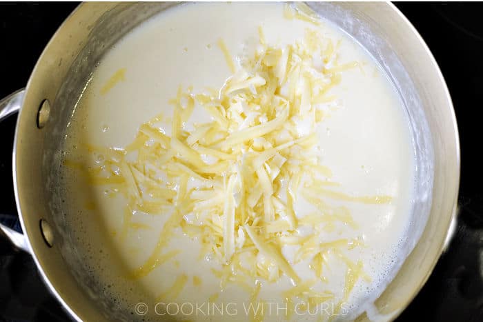 Grated cheese added to the milk mixture in a saucepan.