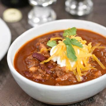 A bowl of chili topped with sour cream, shredded cheddar and cilantro leaves.