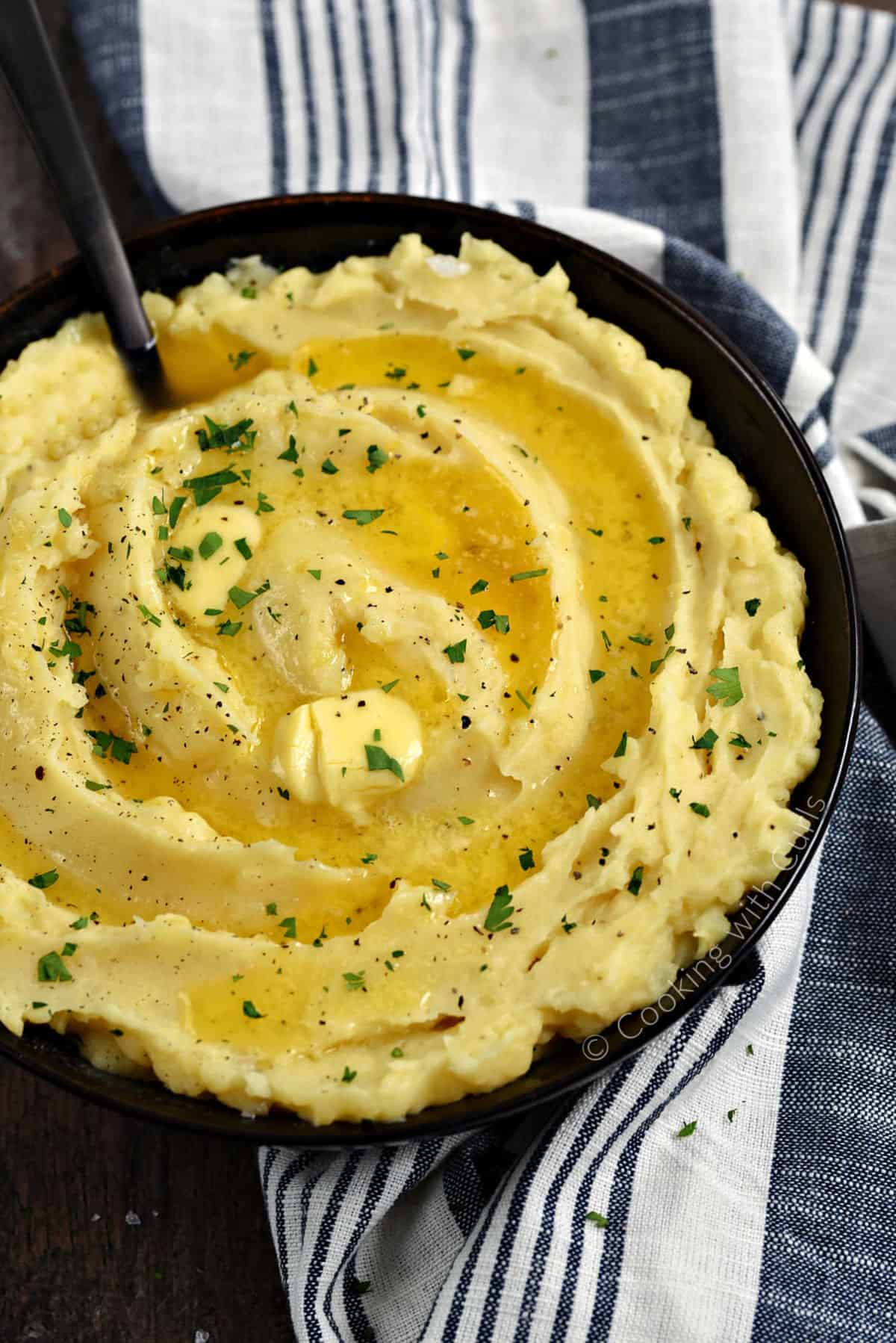 Creamy mashed potatoes topped with melted butter and chopped parsley.