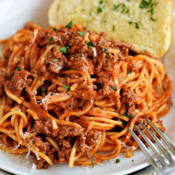 Spaghetti with meat sauce on a white plate with garlic bread on the side.