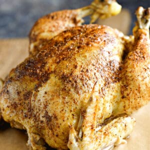 a close-up image of a cooked whole chicken on a wooden cutting board.