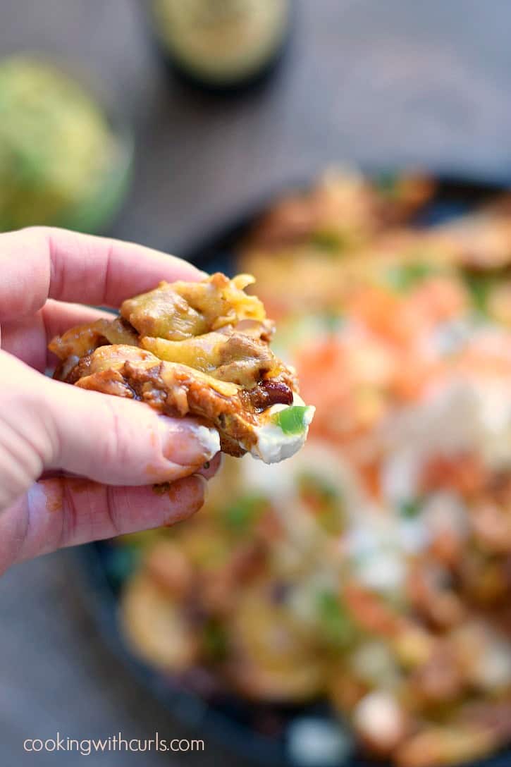 a single potato slice topped with chili and cheese being held and ready to eat