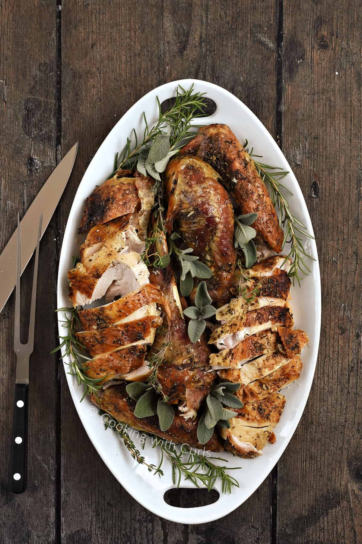 Disassembled turkey on a serving platter with carving knife and fork on the side.