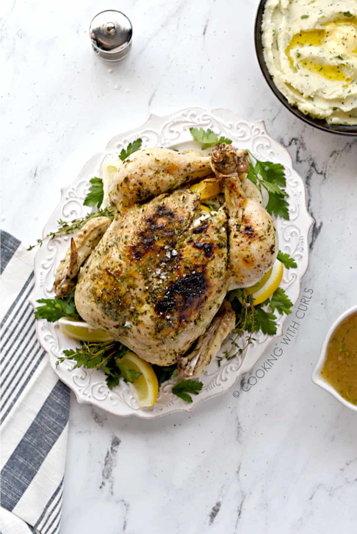 Looking down on a whole chicken with Greek seasonings cooked in an Instant Pot with a bowl of mashed potatoes and gravy in the background. 