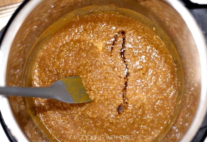 Looking down on pumpkin oatmeal in a pressure cooker while stirring in maple syrup with a gray spoonula. 