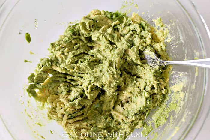 Mashed avocado in a large glass bowl with a fork. 