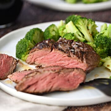 sliced filet mignon on a white plate with broccoli florets, with a second plate in the background.