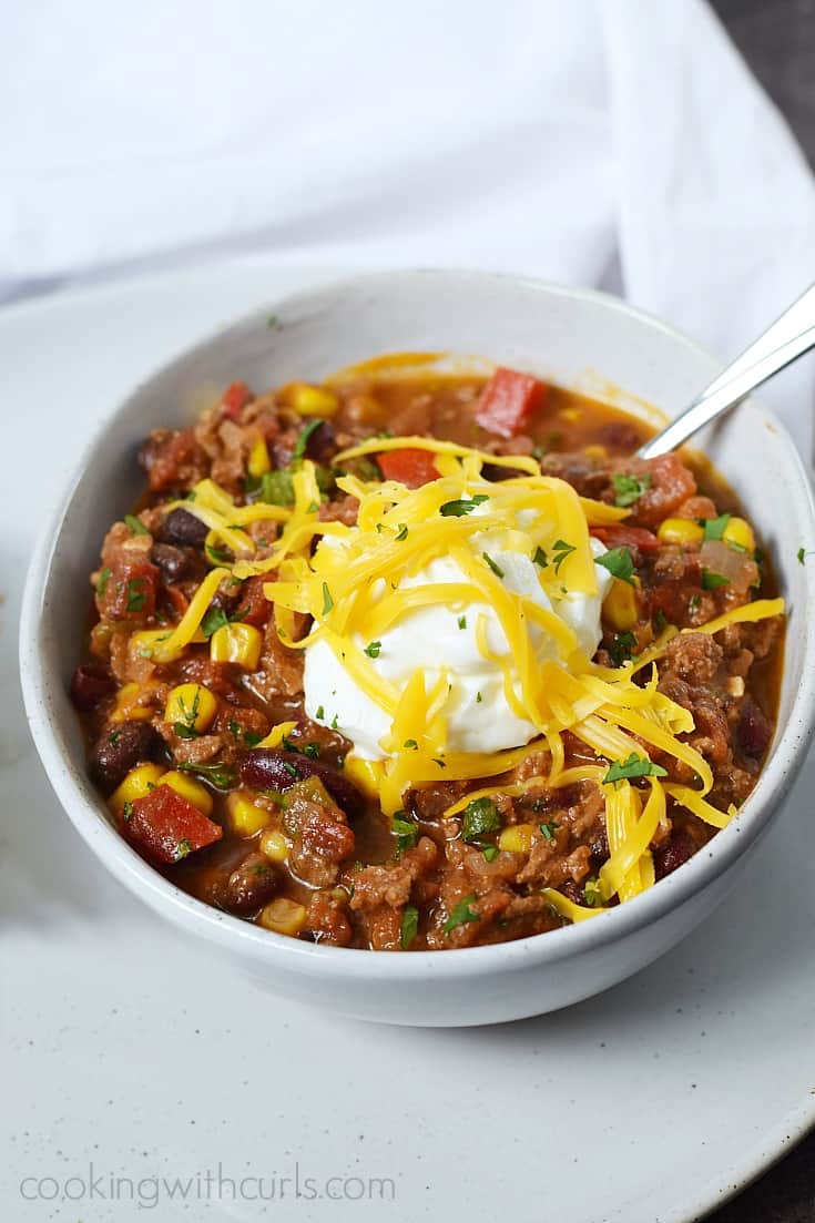 Southwest Chili with Black Beans and Corn topped with sour cream and shredded cheddar cheese in a white bowl.