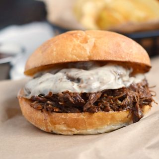 barbecue beef sandwich with melted cheese and potato chips on the side