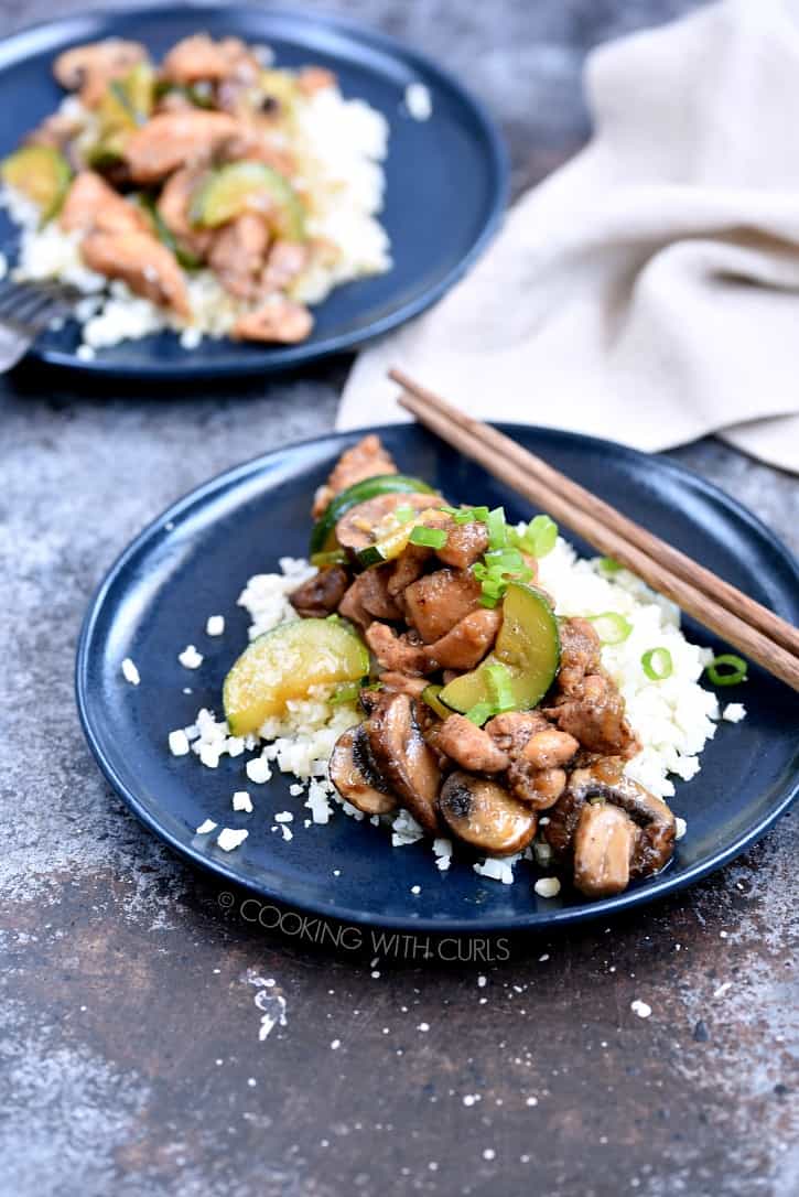 Two blue plates with a bed of rice covered with Instant Pot Chinese Garlic Chicken and wooden chopstick in the upper right hand side of the plate