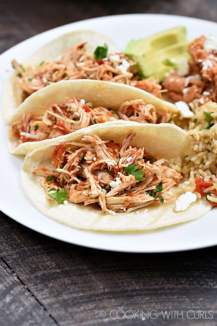 Three tortillas filled with Instant Pot Salsa Chicken on a white plate with refried beans and rice on the side.